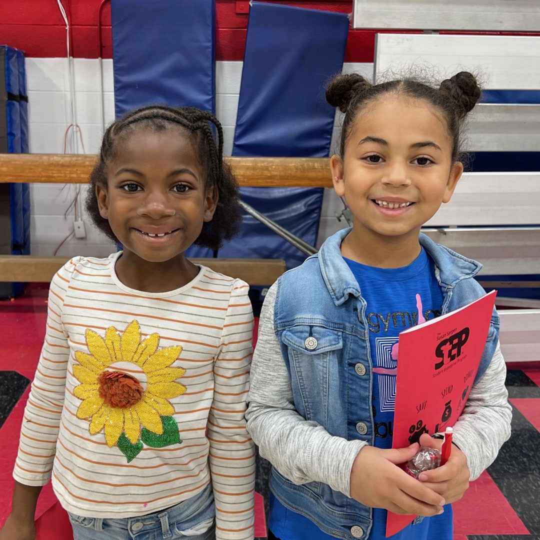 two young children smile while one holds a folder with the word step on the front