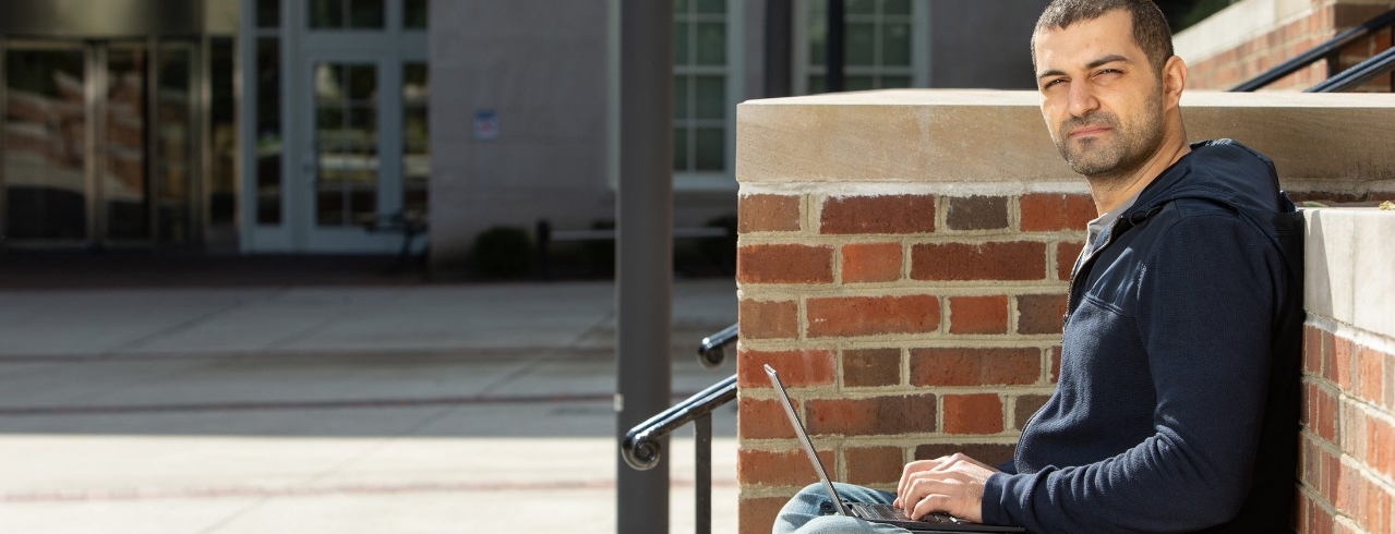 A student works on a laptop on the campus of the University of Cincinnati